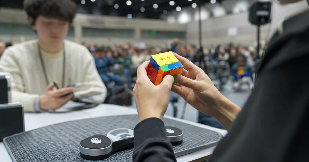 대회 테이블에서 3x3 큐브를 푸는 손, 뒤로 심판과 컨벤션홀 관중이 보인다